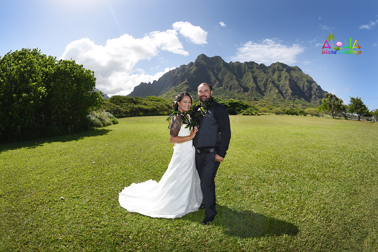 Bride and groom on a green lawn with Oahu's mountains behind them